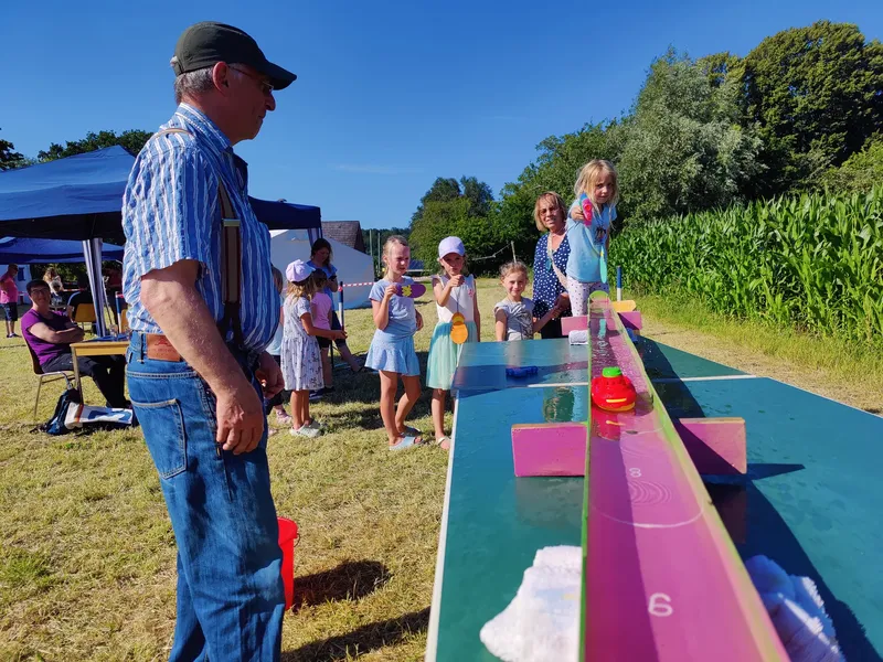 Kinder spielen beim Dorffest ein Wasserspiel mit einer Wasserbahn auf einem Tisch.